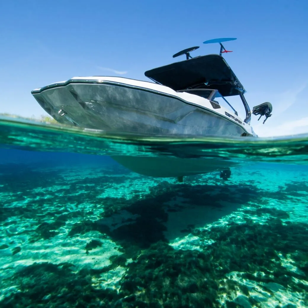 A boat floating on clear, shallow water with a sandy bottom and some underwater vegetation visible. The water is turquoise, and the sky is bright and clear.