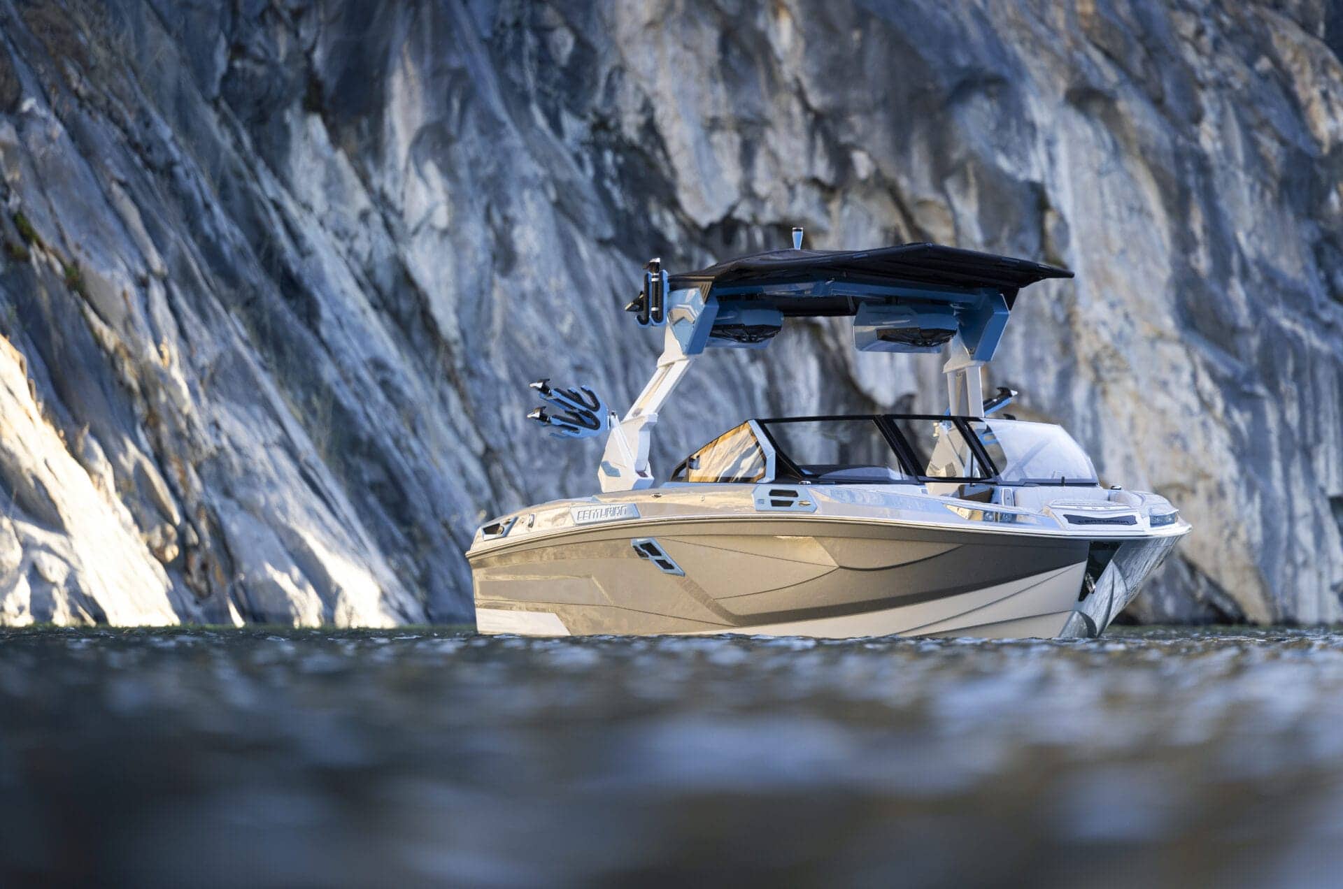 A white and gray boat with a black canopy floats on water against a backdrop of gray rocky cliffs.