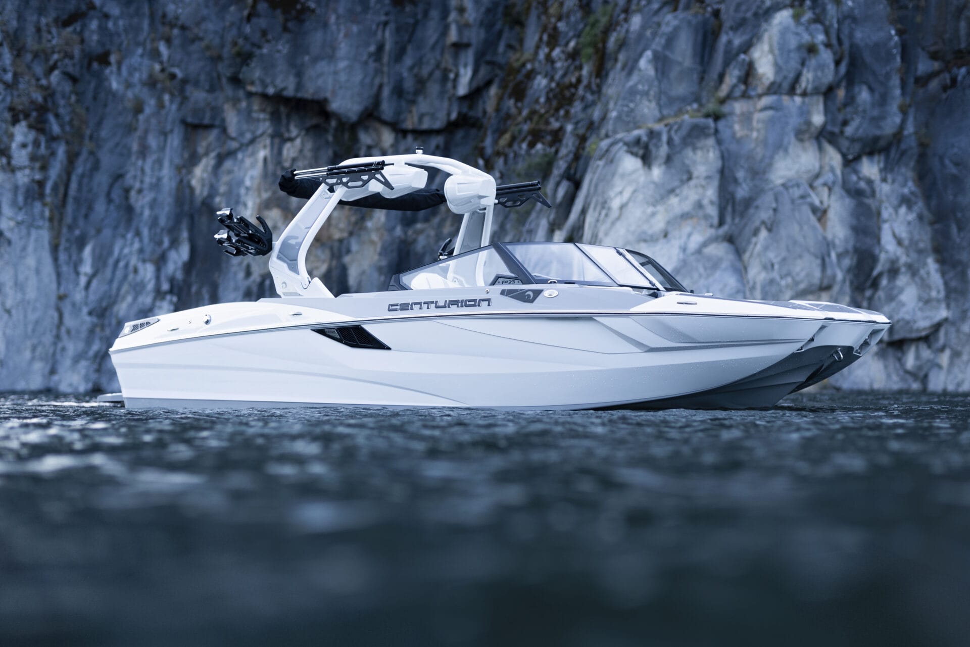 A white Centurion speedboat floats on calm water near a rocky cliff.