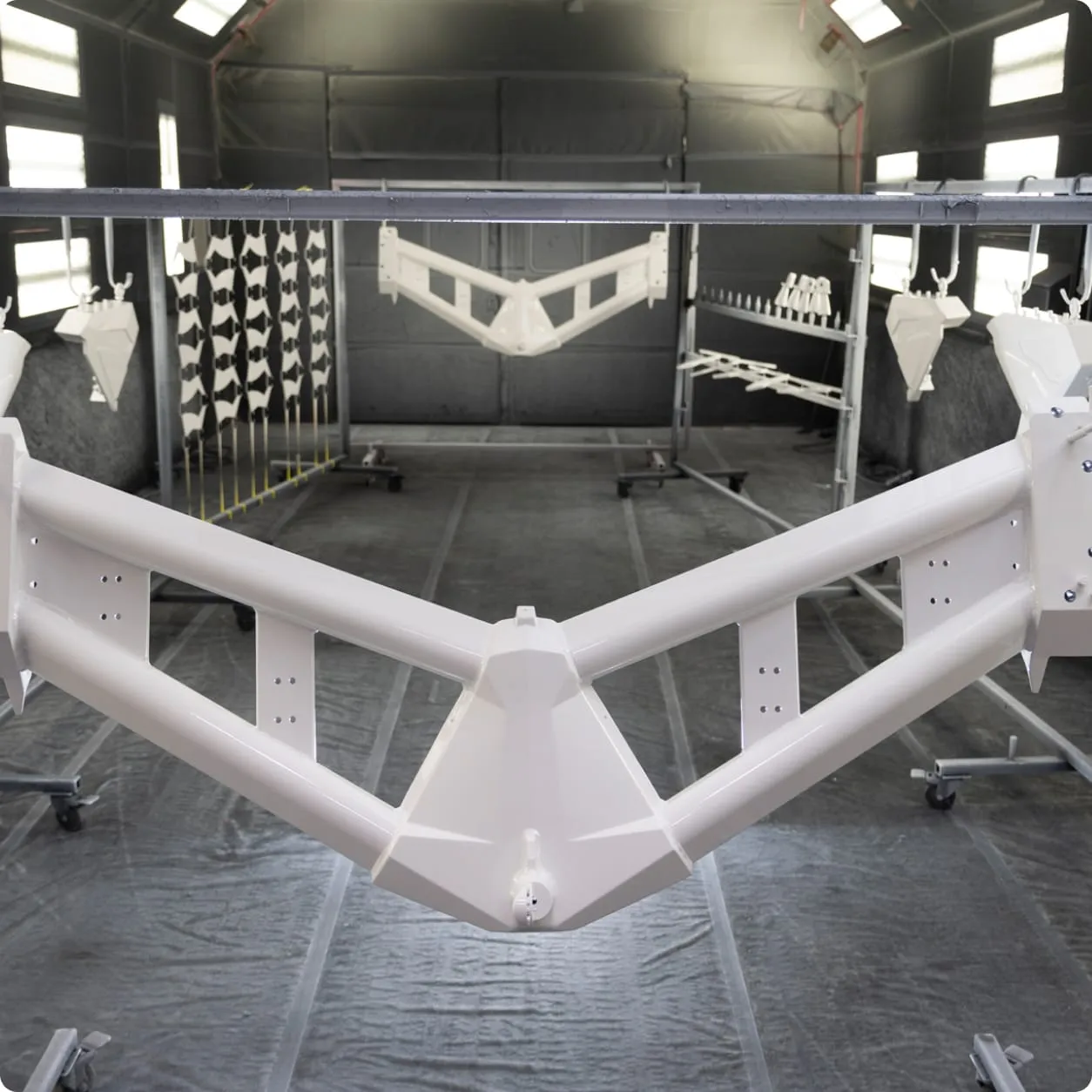 A metal frame coated in white paint hangs in a spray booth alongside other Centurion Towers components, drying in a controlled environment.