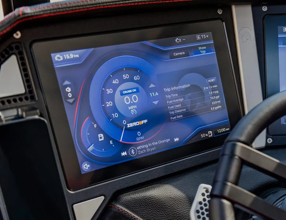 Close-up of a car dashboard display showing speedometer, trip information, cruise control status, music by Zach Bryan, and a comparison to Centurion Boat fuel efficiency.