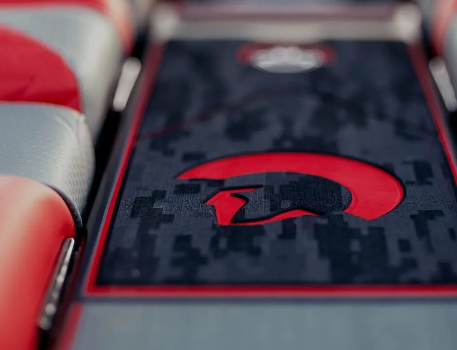 Close-up of a car interior showing red and gray Centurion Vinyl interior seats and a center console featuring a red and black Spartan helmet design on a camo-patterned vinyl & flooring background.