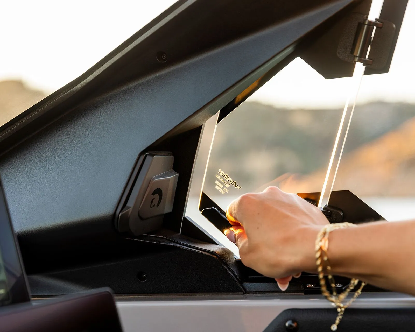A person opens a small window on a Centurion Nv Series vehicle dashboard, with sunlight reflecting off their bracelet and the edges of the glass.