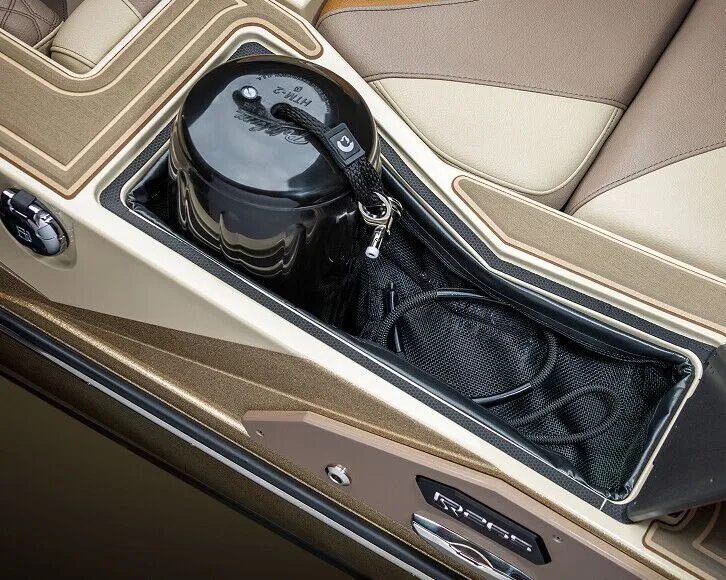 A black bucket with a strap and a coiled rope sits in a mesh storage compartment between beige and brown boat seats on one of the Centurion Nv Series Surf Boats.
