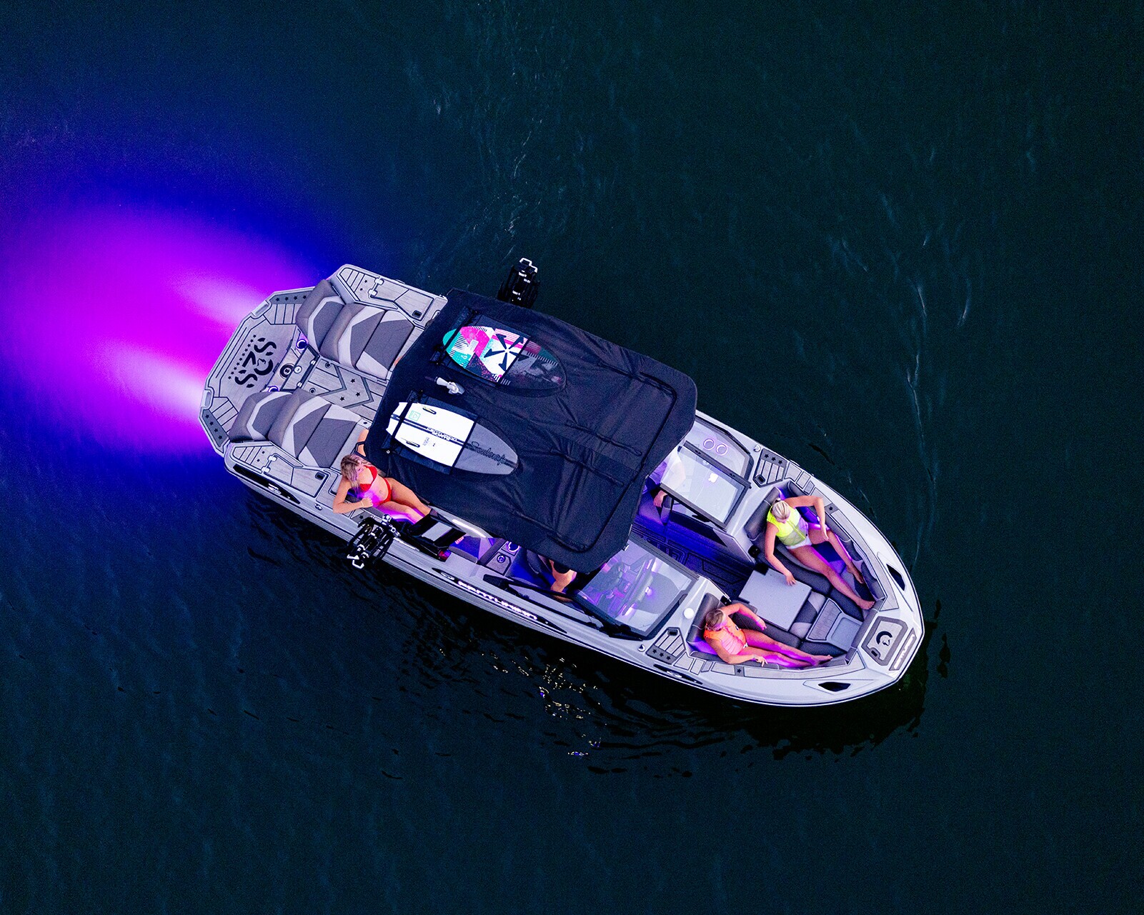 Overhead view of a Centurion Ri230 Wake Boat with four people on board, traveling on dark water, with purple light glowing from the rear.
