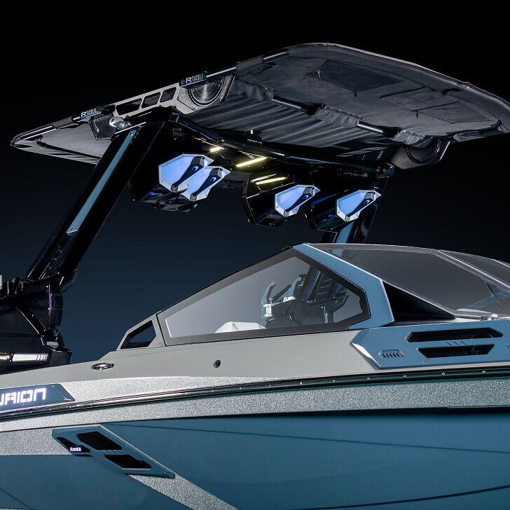 A close-up view of a modern powerboat with a black wakeboard tower equipped with speakers and a bimini top against a dark background.