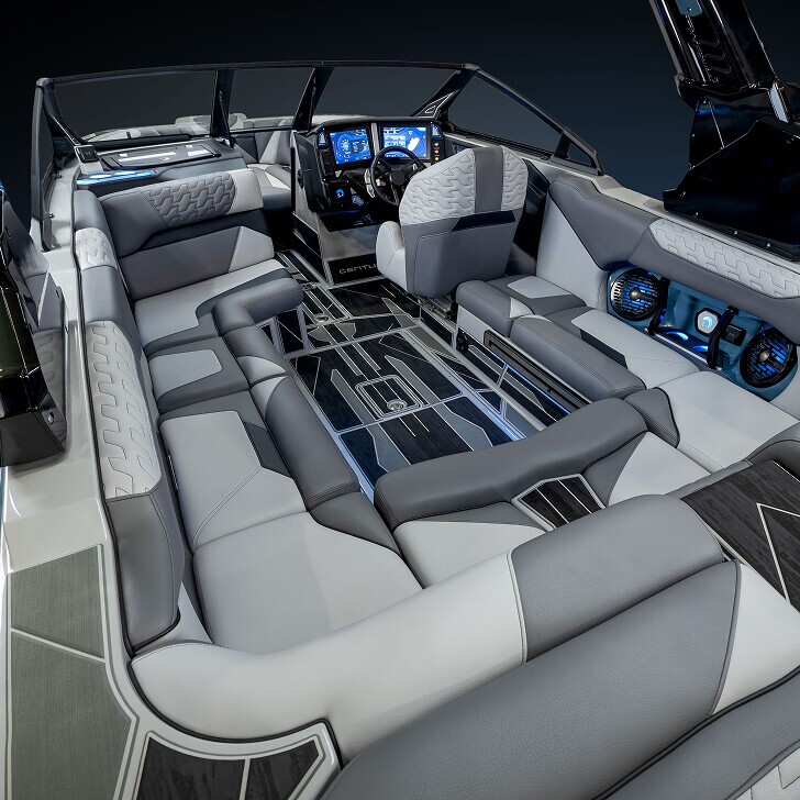 Interior of a modern speedboat featuring gray and white cushioned seating, digital dashboard, built-in speakers, and sleek, geometric flooring.