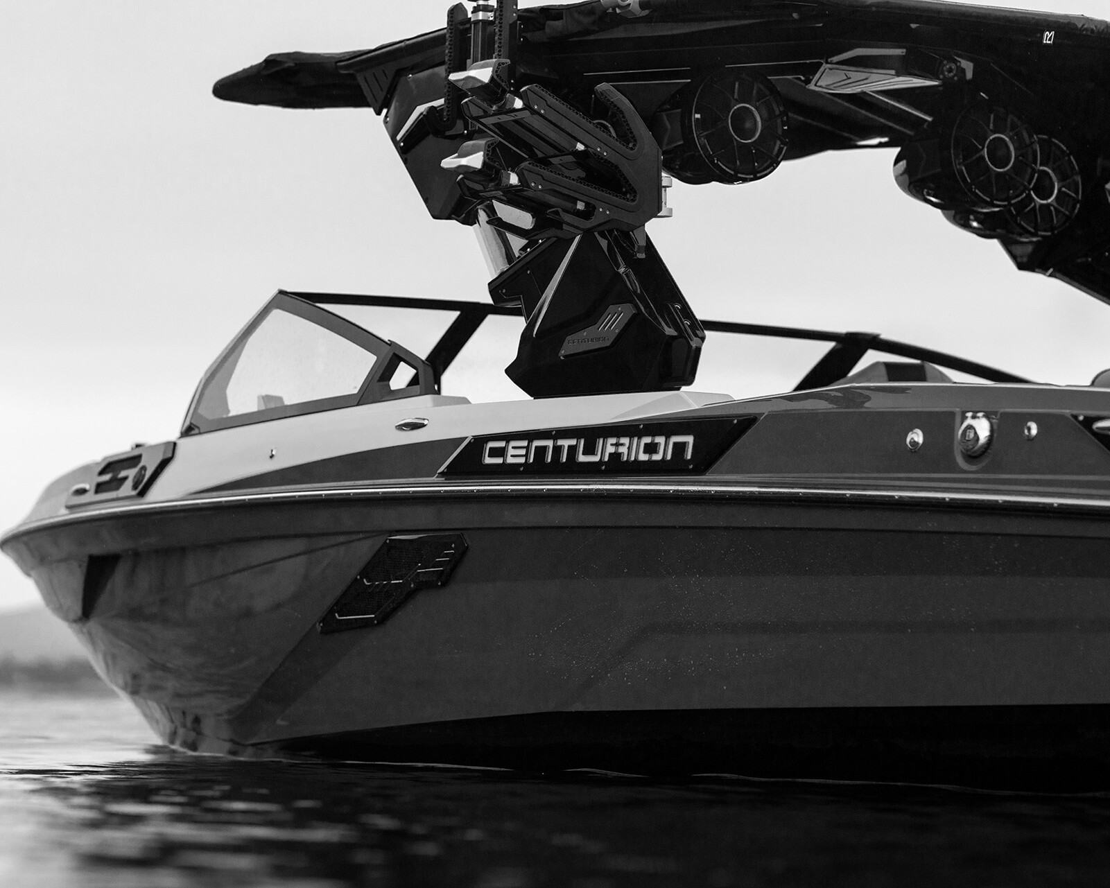 A black and white photo shows the front side of a Centurion Ri245 Surf Boat on calm water.