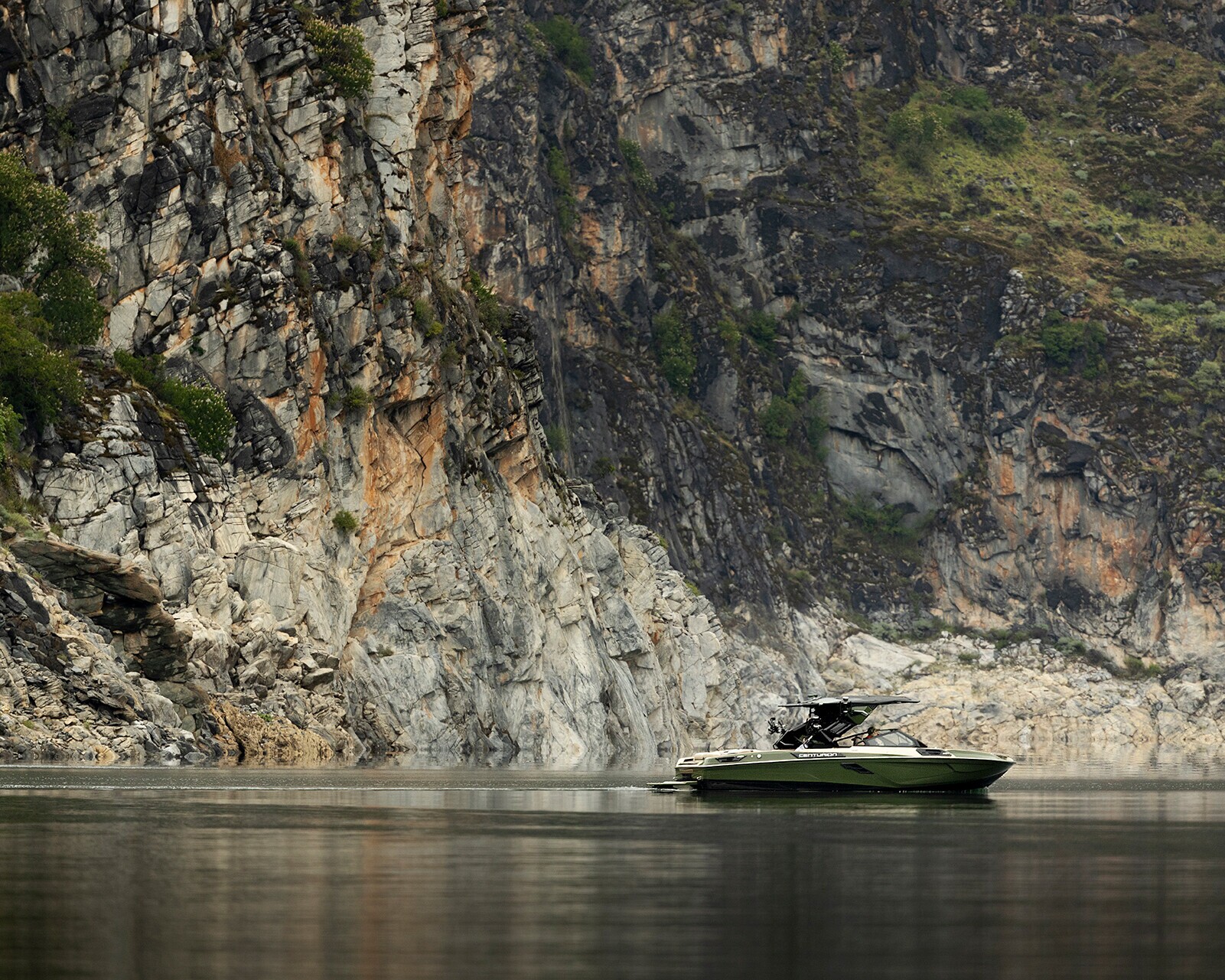 A Centurion Ri245 motorboat floats on calm water near steep, rocky cliffs with patches of greenery.