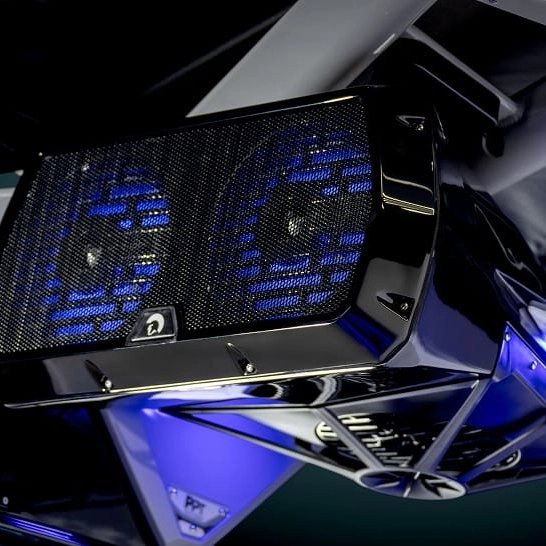 Close-up view of a black and chrome Ri Series dual speaker system with blue LED lighting, mounted under a surface. Features personal audio controls for a tailored listening experience.