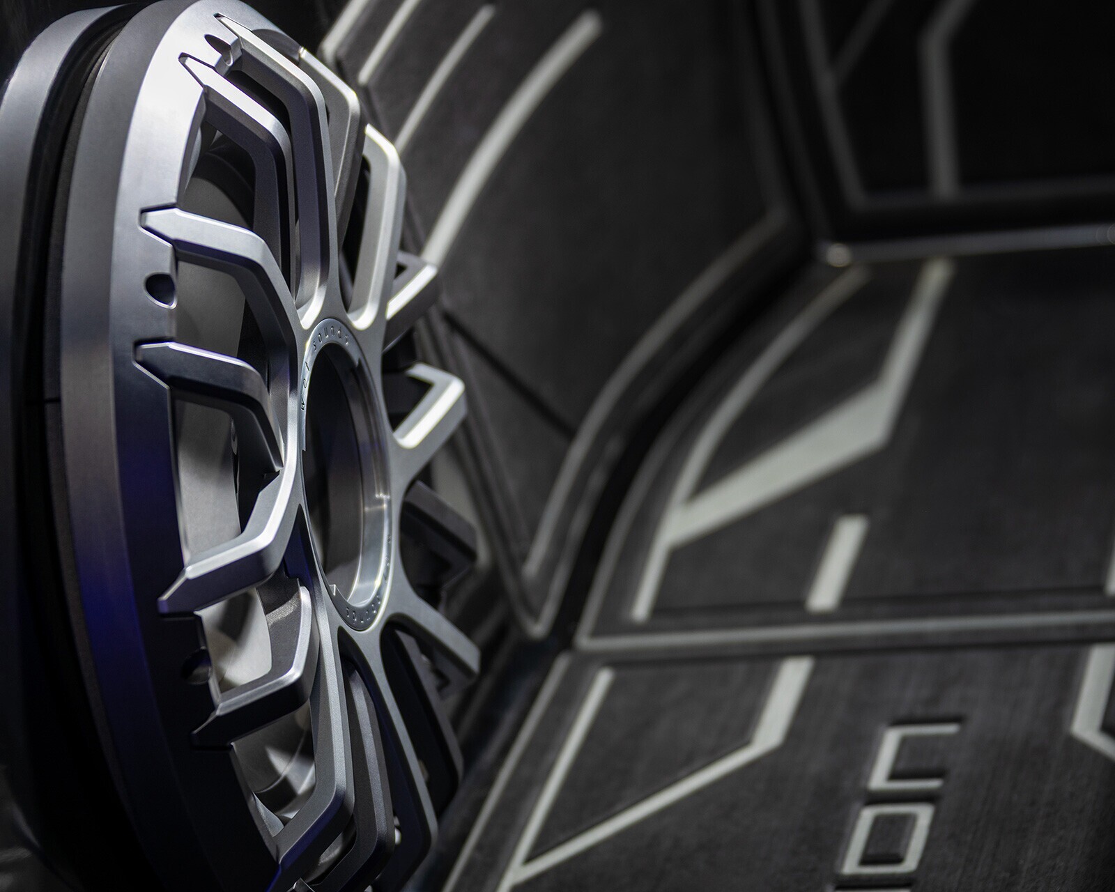 Close-up view of a silver alloy car wheel rim mounted on a dark, geometric-patterned background, resembling the modern design seen on Centurion Nv243 models.