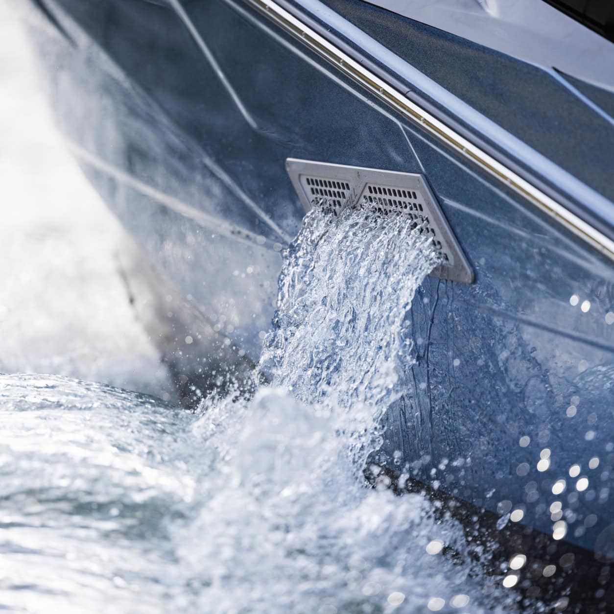 Close-up of water pouring out of a rectangular drain on the side of a boat into the surrounding water.