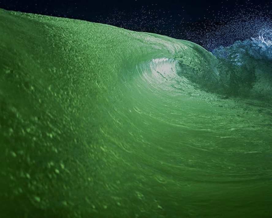 A close-up view of a green Centurion surf wave curling and splashing under a dark sky.