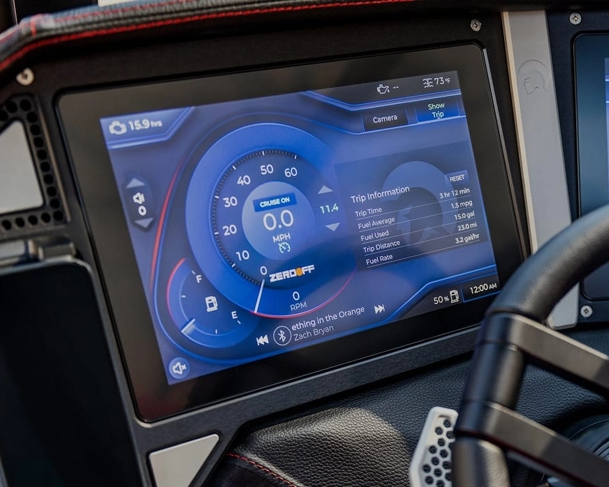 Close-up of a car dashboard display showing speedometer, trip information, cruise control status, music by Zach Bryan, and a comparison to Centurion Boat fuel efficiency.