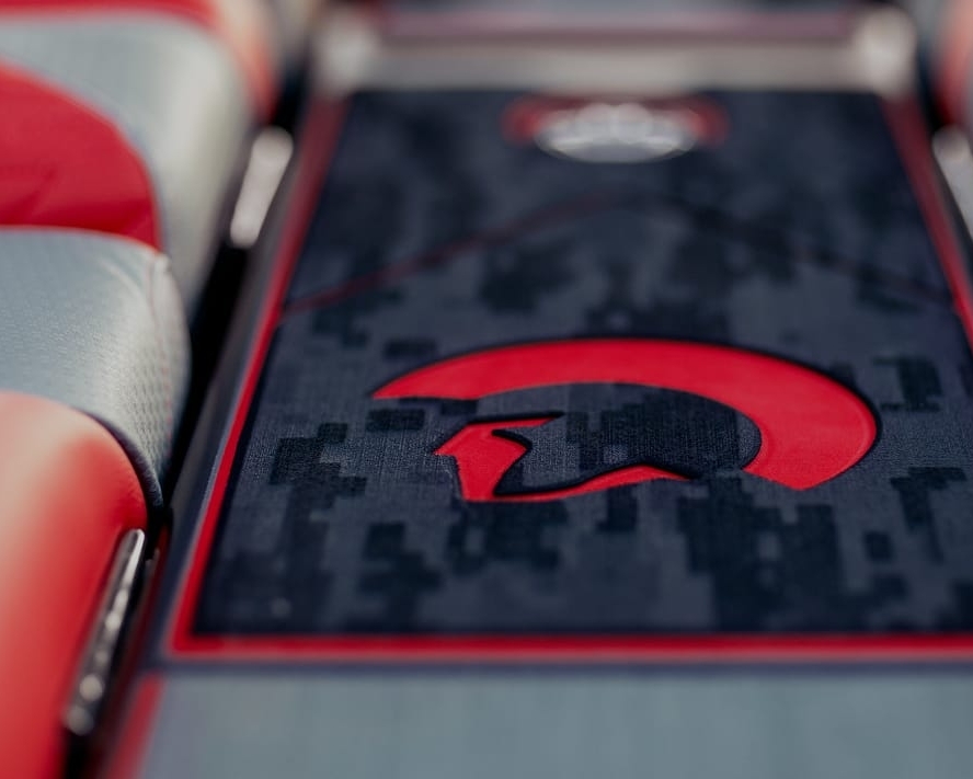 Close-up of a car interior showing red and gray Centurion Vinyl interior seats and a center console featuring a red and black Spartan helmet design on a camo-patterned vinyl & flooring background.