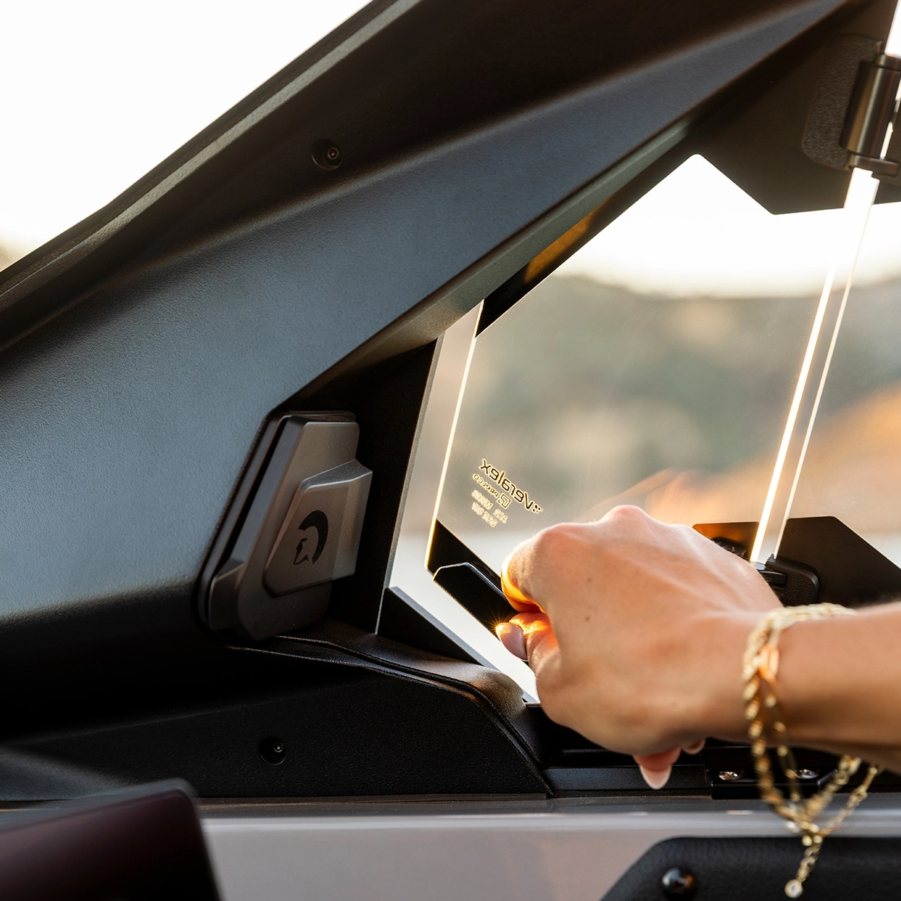 A person opens a small window on a Centurion Nv Series vehicle dashboard, with sunlight reflecting off their bracelet and the edges of the glass.