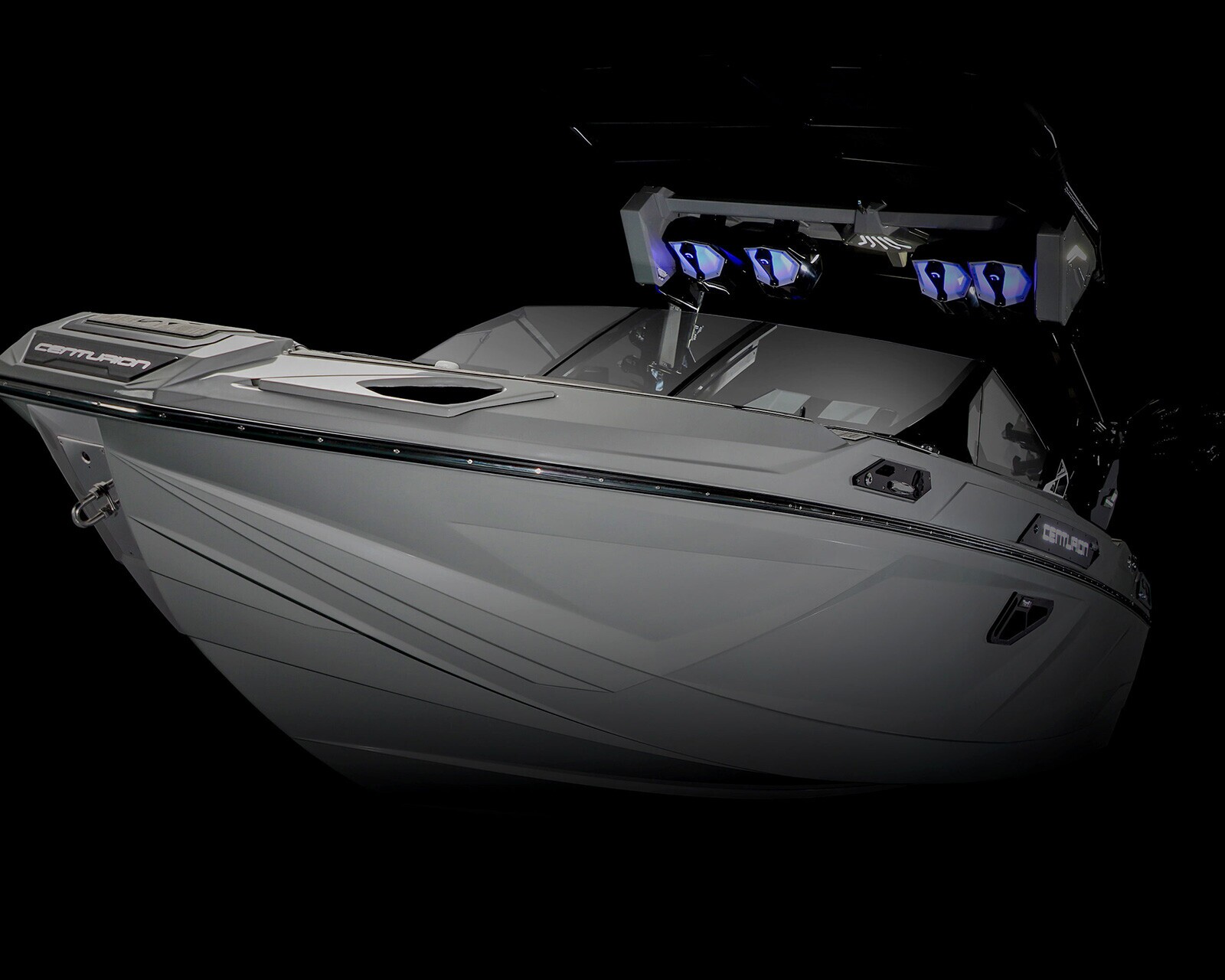 A modern, gray Centurion speedboat with angular lines and blue lights on the overhead speakers, pictured against a black background.