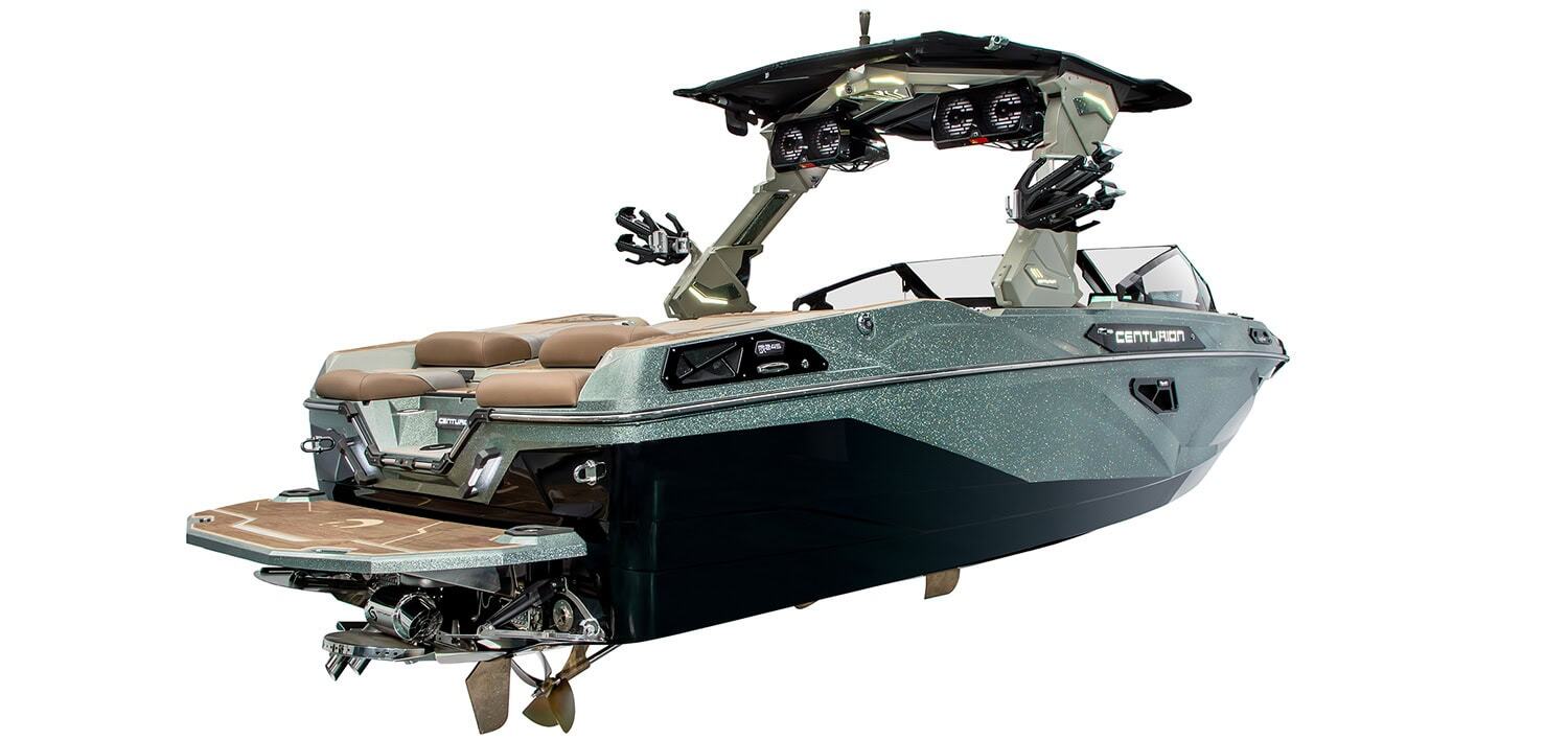 A modern wakeboarding boat with brown seating, black hull, metallic green detailing, and tower speakers is shown from the rear and side angle.
