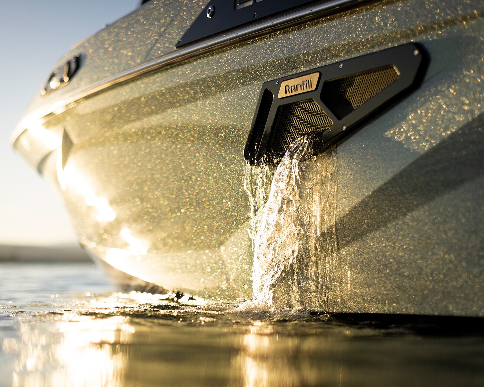 Close-up of water pouring out of a designated exhaust port on the side of a boat, with sunlight reflecting off the boat's surface.