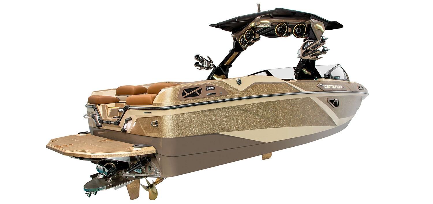 A modern luxury wakeboard boat with brown and tan color scheme, exposed speakers, and seating, viewed from the rear left side against a white background.