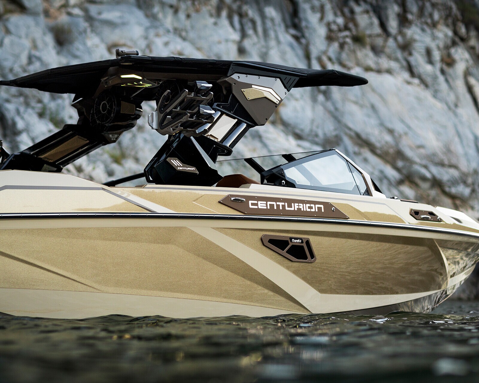 A gold Centurion speedboat floats near rocky cliffs, with its canopy and wakeboard racks visible above the waterline.