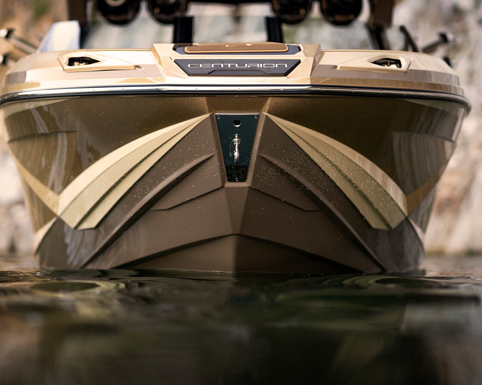 Close-up of the bow of a Centurion boat on the water, with geometric patterns and a chrome logo visible above the waterline.