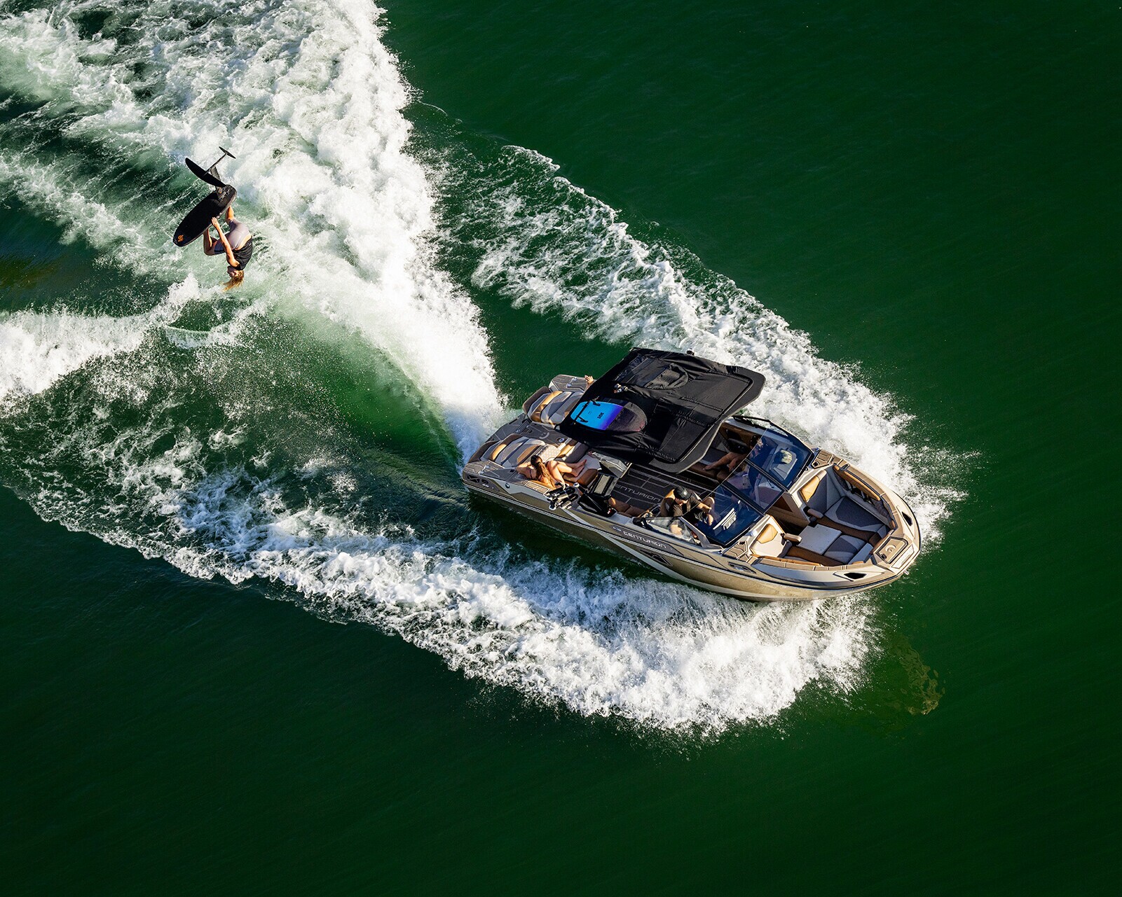A person wakeboards behind a motorboat on green water, creating white waves as the boat moves forward.