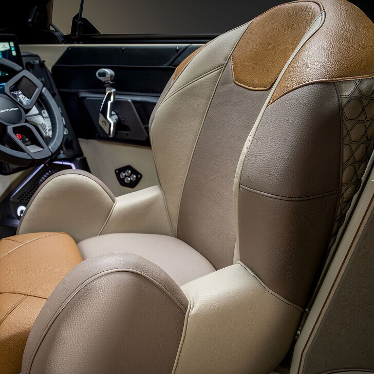 A close-up of a brown, beige, and tan leather boat captain’s chair with padded armrests, visible stitching, and part of the steering wheel and dashboard in the background.