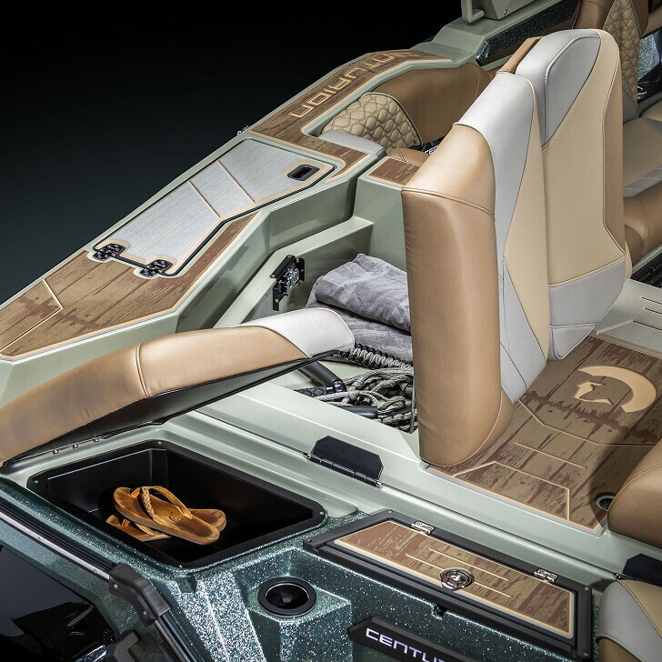 Open storage compartments in a boat's cockpit reveal towels, a rope, and sandals. The boat features brown and beige cushioned seats and wood-patterned flooring.