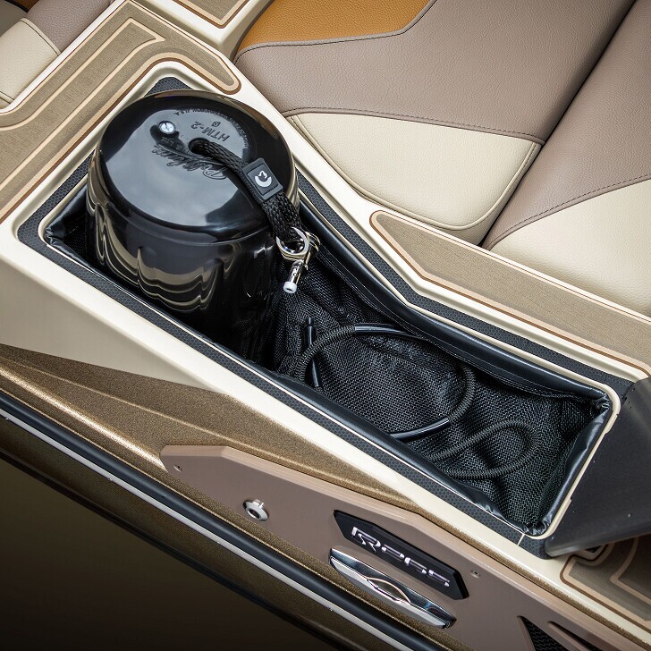 A black container attached with a strap sits in a mesh-lined compartment between tan and brown car seats.