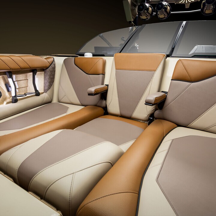 Brown and beige leather seats with armrests and built-in speakers in a modern Centurion Nv Series boat interior, seen from the rear facing forward.
