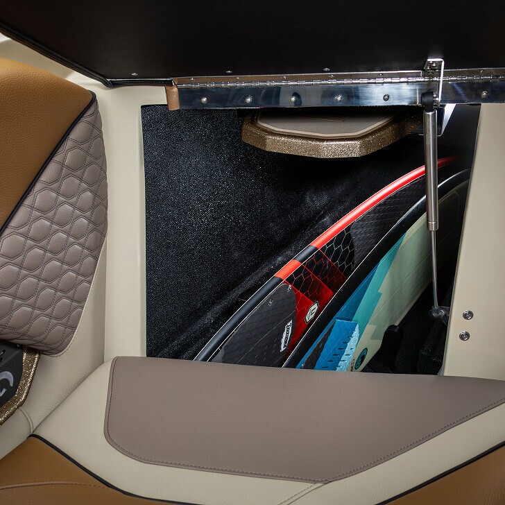 Boat storage compartment containing surfboards, shown with seats upholstered in tan, cream, and quilted brown leather.