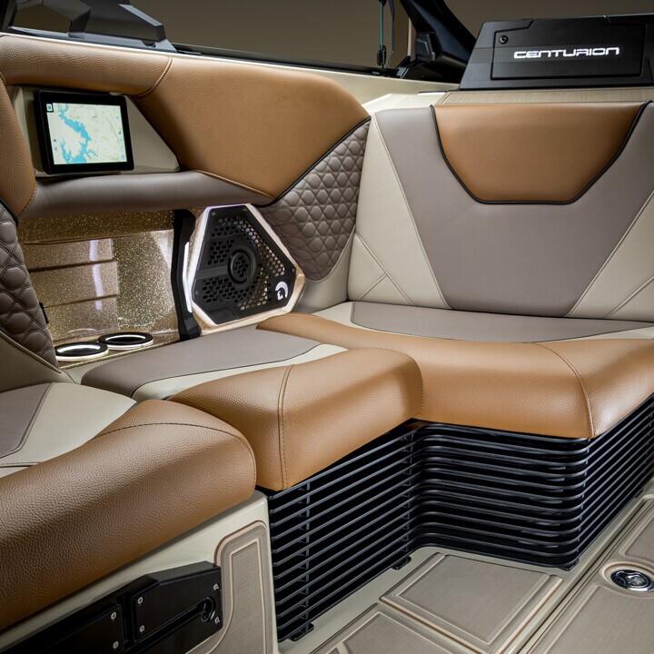 Brown and beige leather seats on a luxury boat interior, featuring quilted stitching, cup holders, a speaker, and a small display screen.