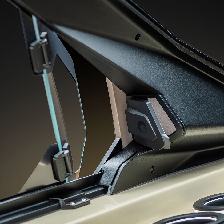 Close-up of a glass window with a metal hinge and latch mechanism attached to a black and beige frame; focus on the structural details and materials.