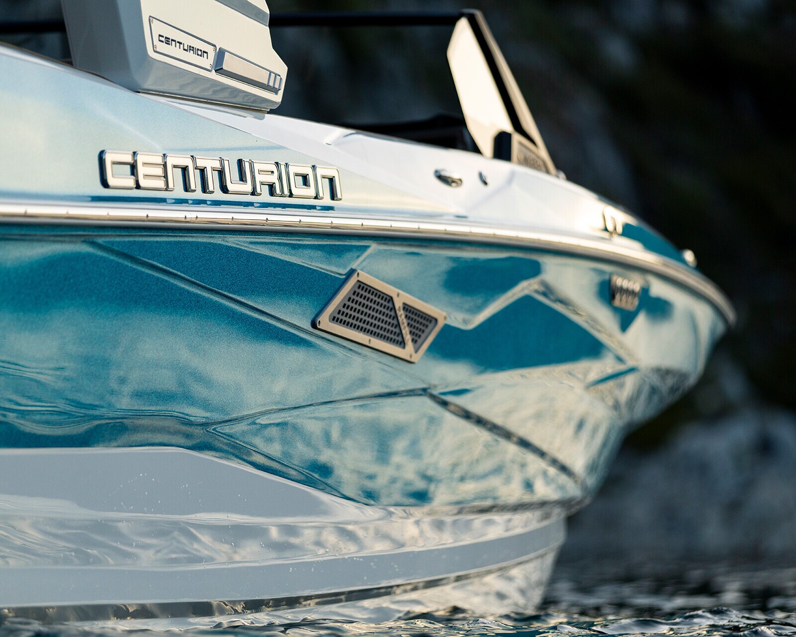 Close-up of the bow of a blue and white Centurion Nv243 Surf Boat, showing the brand logo and part of the hull above water.