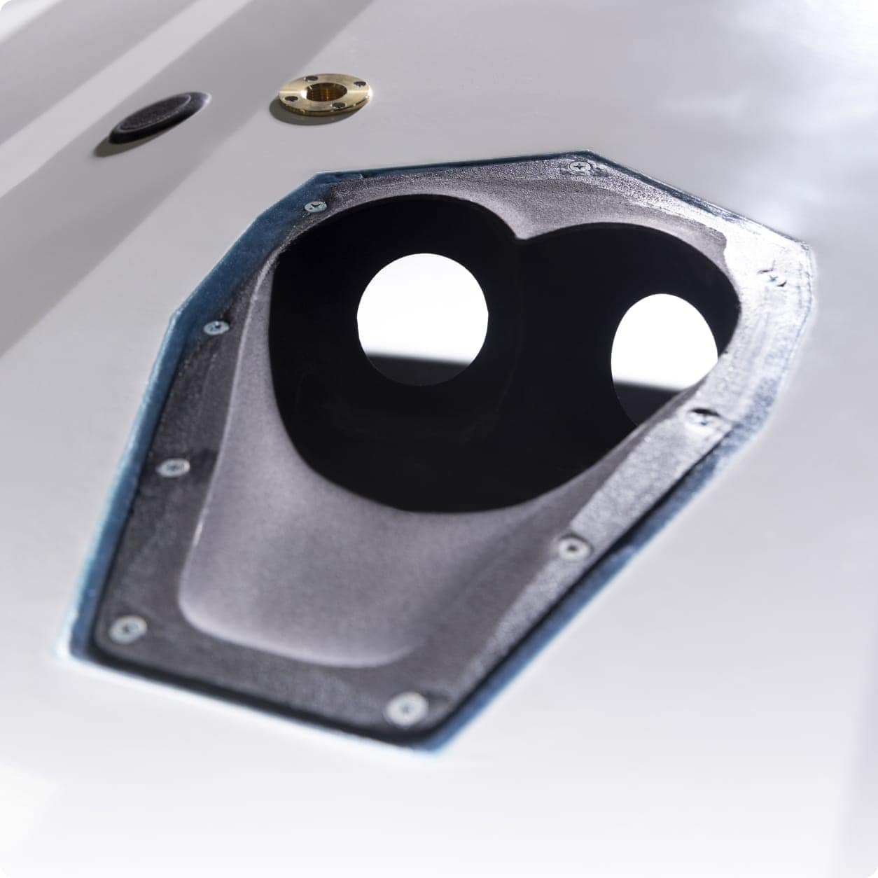 Close-up of a Centurion RAMFILL black, oval-shaped opening with two circular holes on a white surface, bordered by screws and a blue lining.
