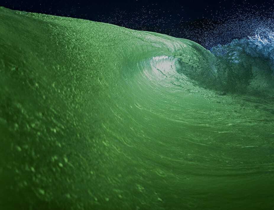 A close-up view of a green Centurion surf wave curling and splashing under a dark sky.