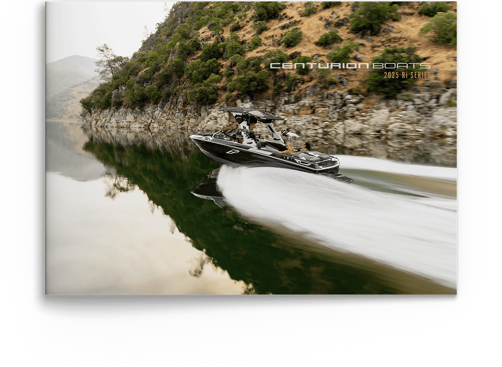 A black speedboat moves quickly across a calm, narrow lake with rocky hills and trees on the shore; water is smooth, leaving a wake behind. Discover Centurion Boats&mdash;text reads 
