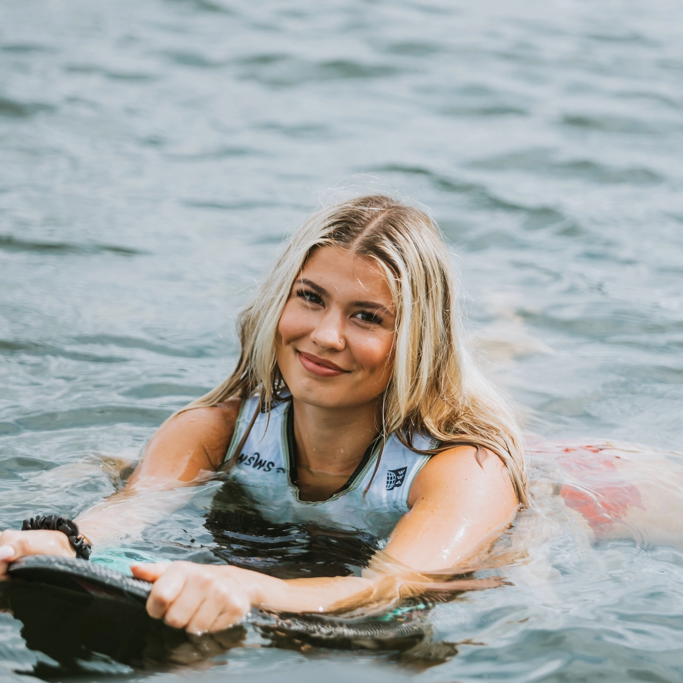 Woman smiling while floating in the water and holding a wakesurf board.