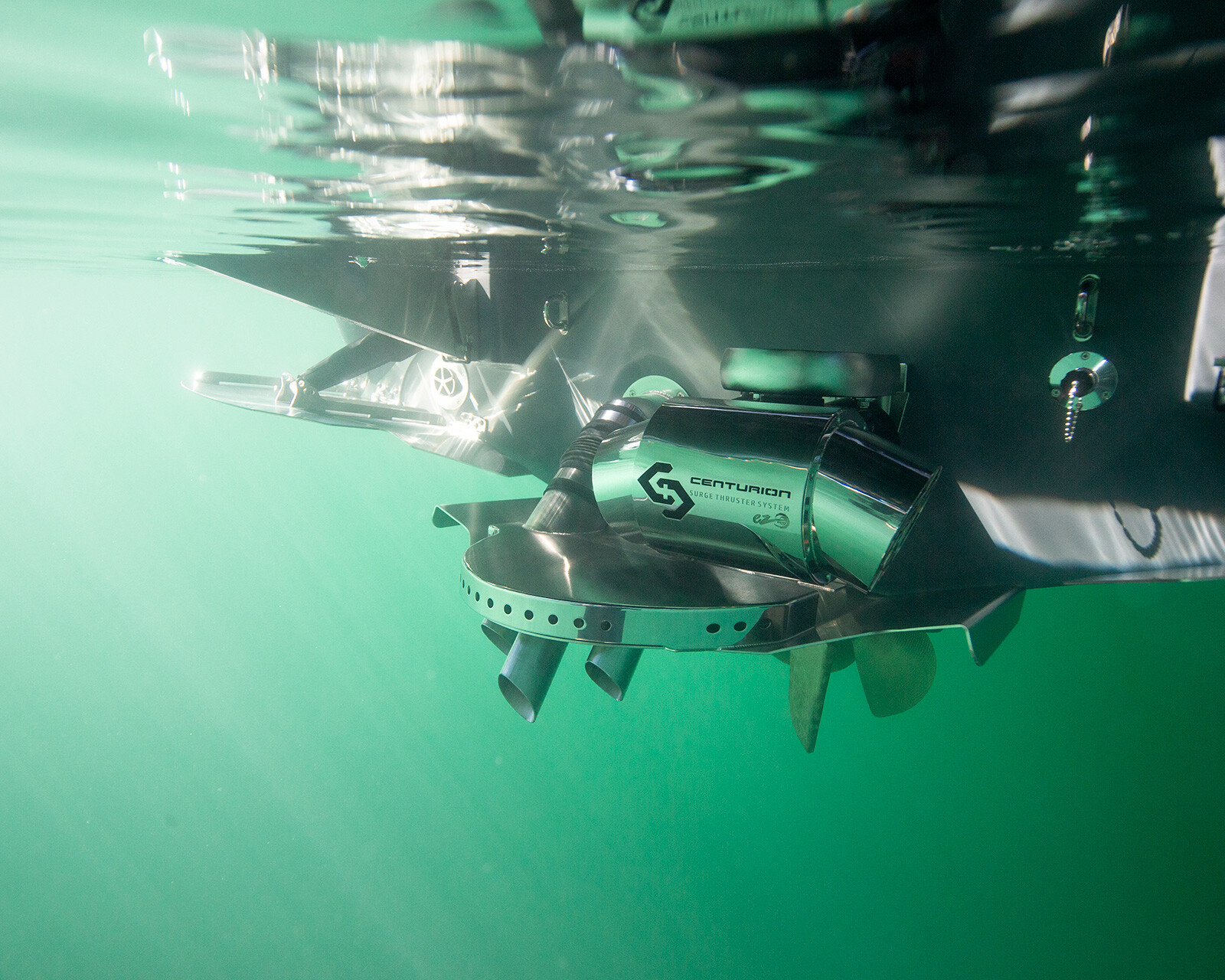 Close-up view of a Centurion Ri230 surf boat propeller partially submerged in greenish water, reflecting light and metal parts above and below the surface.