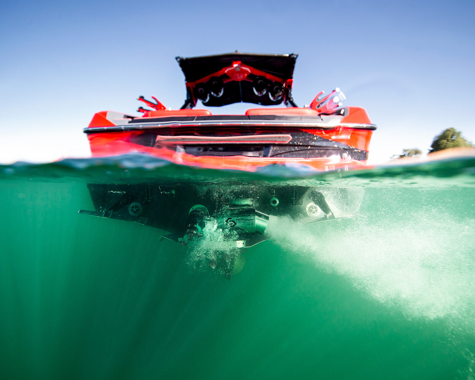 A split-level view showing the back of a red Centurion Ri230 Surf Boat on the water, with part of the boat and its motor visible underwater.