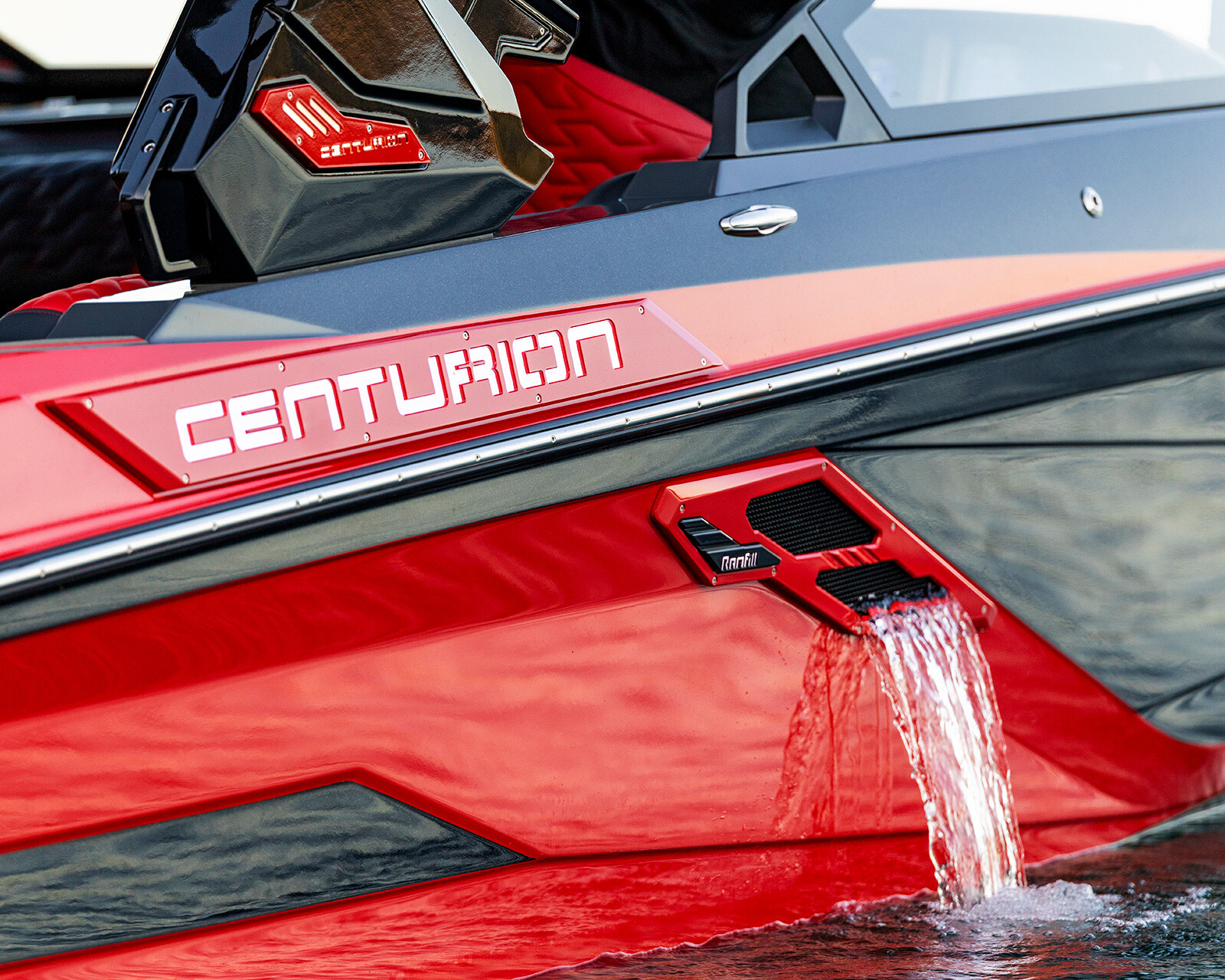 Close-up of a red and black Centurion Ri230 on the water, with water flowing out of a side vent near the boat's stern.
