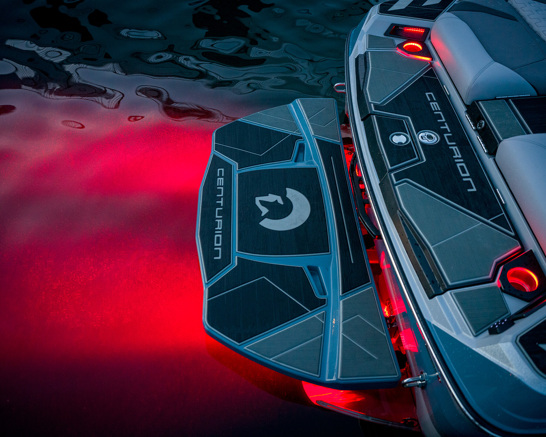 Rear deck of a Centurion Ri230 Surf Boat illuminated by red underwater lights, with the Centurion logo visible on the platform and step.