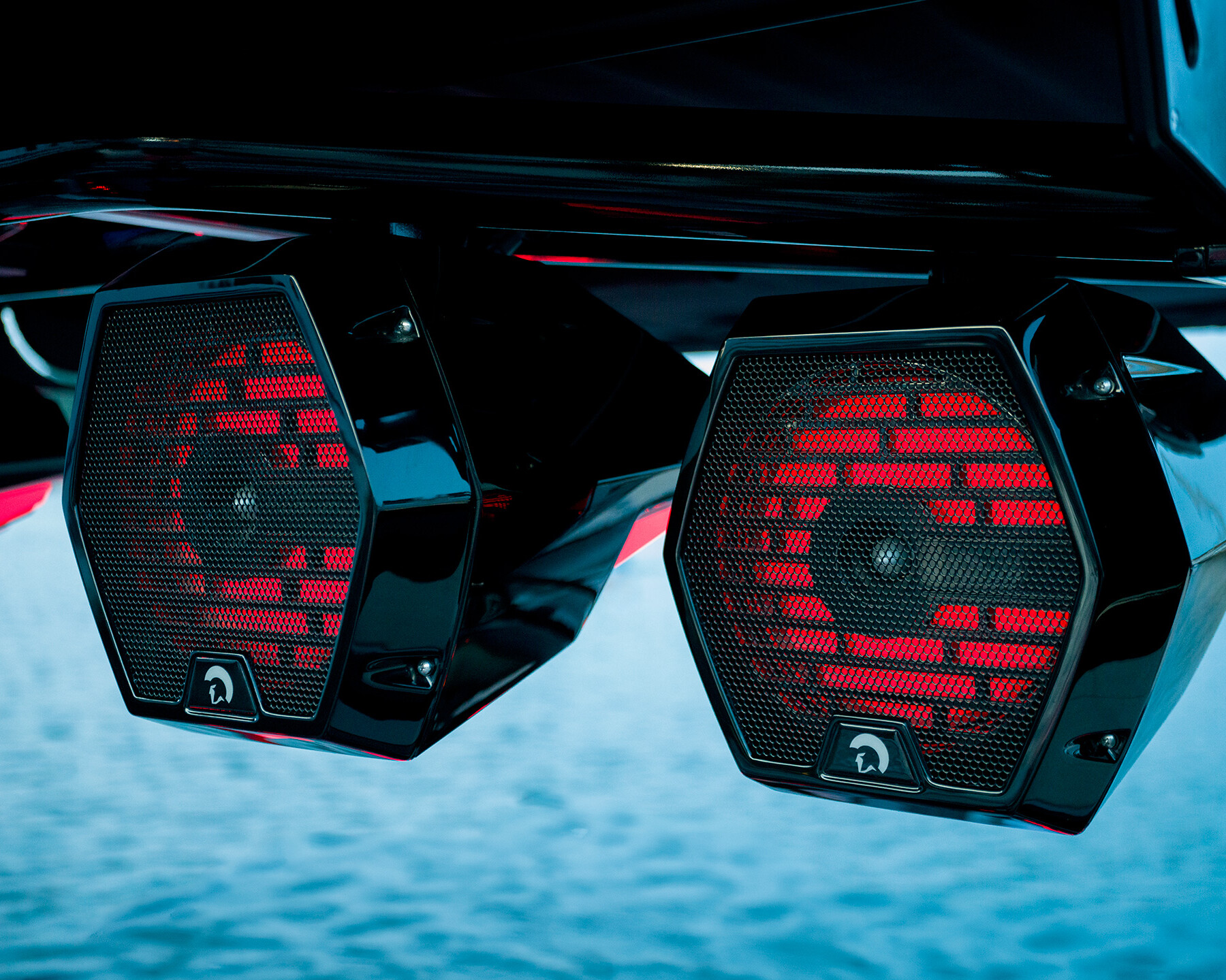 Close-up of two black, hexagonal speakers with red lighting, mounted above a body of water on a Centurion Ri230 Surf Boat.