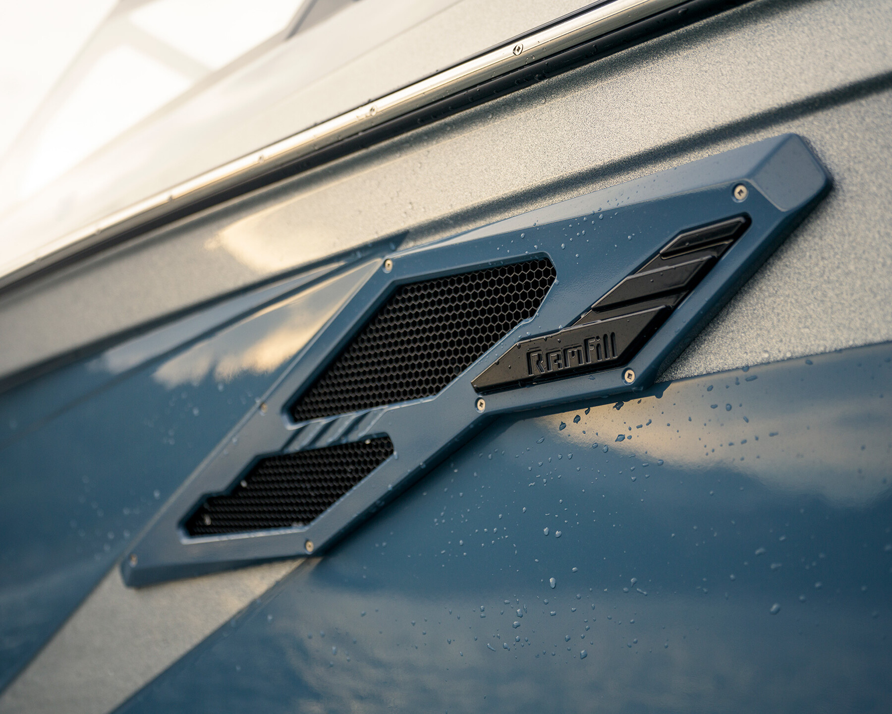 Close-up of a blue and gray Centurion Ri230 exterior featuring a sleek black Ramfill vent with water droplets on the surface.