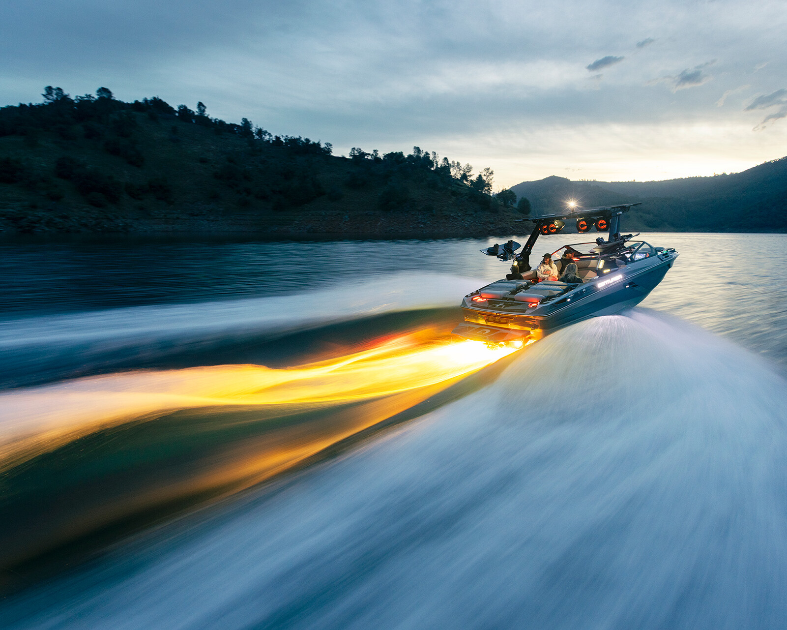 A Centurion Ri230 speedboat moves quickly across a lake at sunset, with bright orange lights creating a glowing trail behind it.