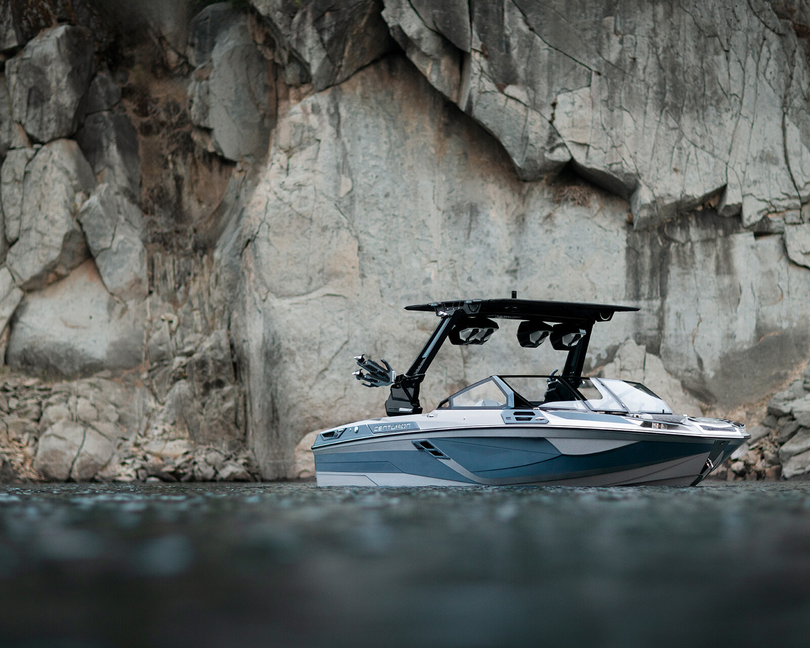 A white and blue Centurion Ri230 floats on calm water near a rocky cliff face.