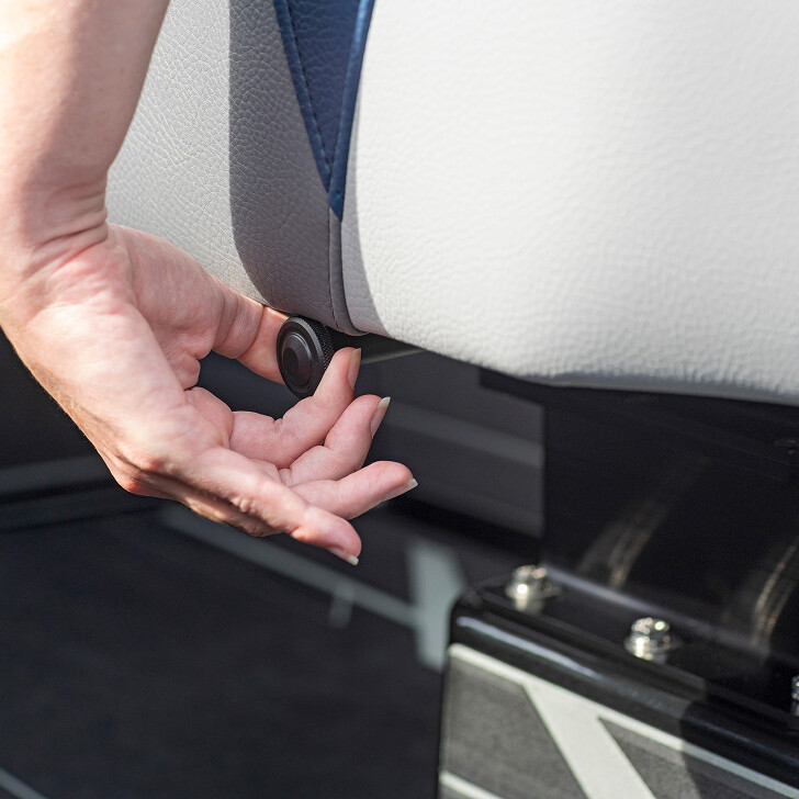 A person adjusts a knob located under a light gray upholstered seat.