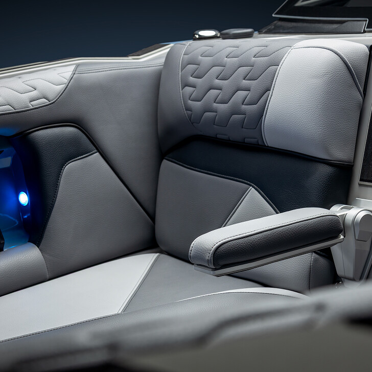 Close-up of a modern car seat with grey and black upholstery, quilted pattern on the backrest, and an adjustable padded armrest.