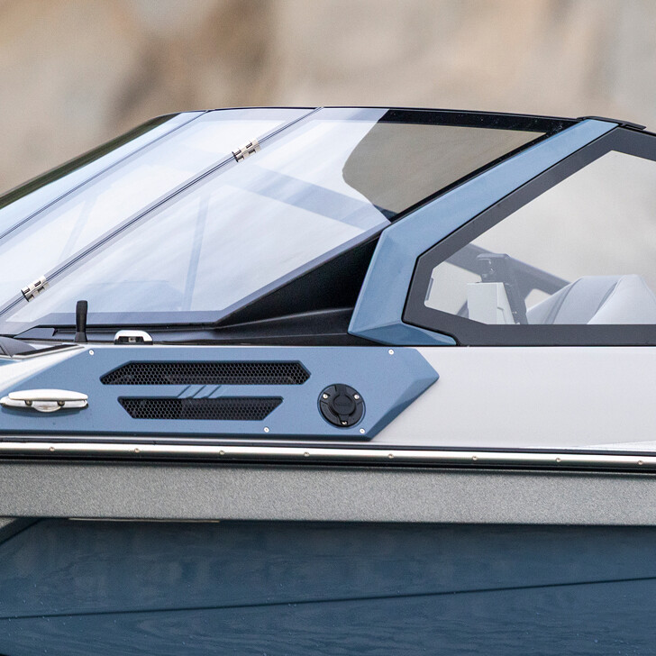 Close-up of the side of a modern boat showing part of the windshield, window, and seating area with a blue and gray color scheme.